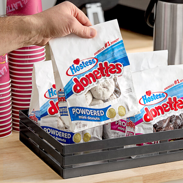 A person's hand holding a bag of Hostess Powdered Sugar Mini Donuts.