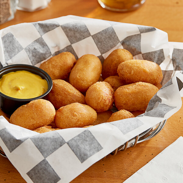 A basket of Foster Farms Mini Chicken Corn Dogs with a bowl of mustard on a table.