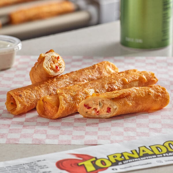 A group of fried Ruiz Foods Cheesy Pepper Jack Tornado Taquitos on a checkered table.