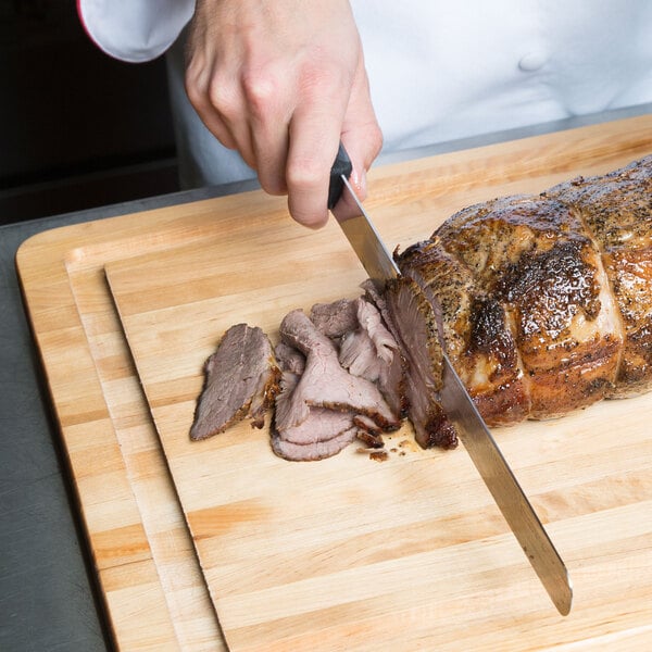 A person using a Victorinox 12" slicing / carving knife to cut meat on a cutting board.