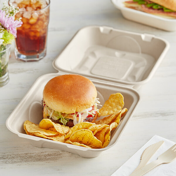 A World Centric compostable fiber clamshell with a burger and chips inside.