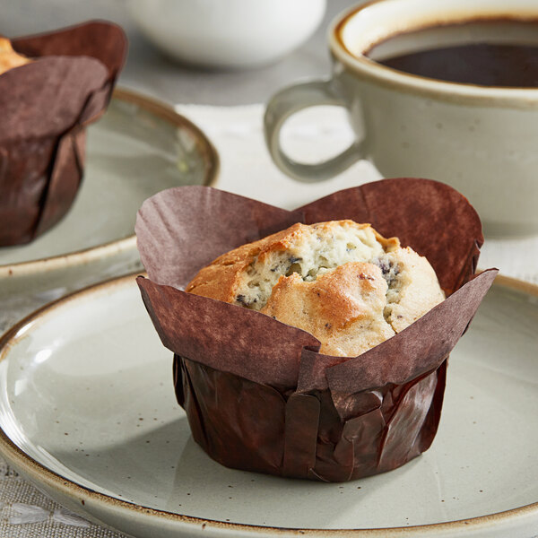 Two Baker's Mark chocolate brown muffins on a plate with a cup of coffee.