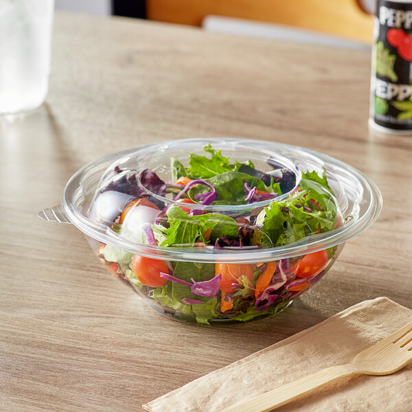 A clear plastic bowl filled with salad and a lid with a wooden fork on a table.