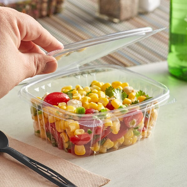 A hand holding a Stalk Market clear plastic deli container of corn and tomatoes.
