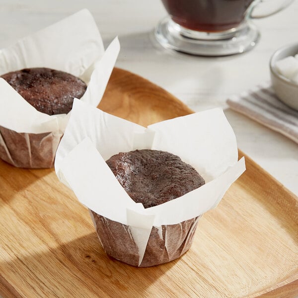 Two brown muffins wrapped in white paper on a wooden tray.