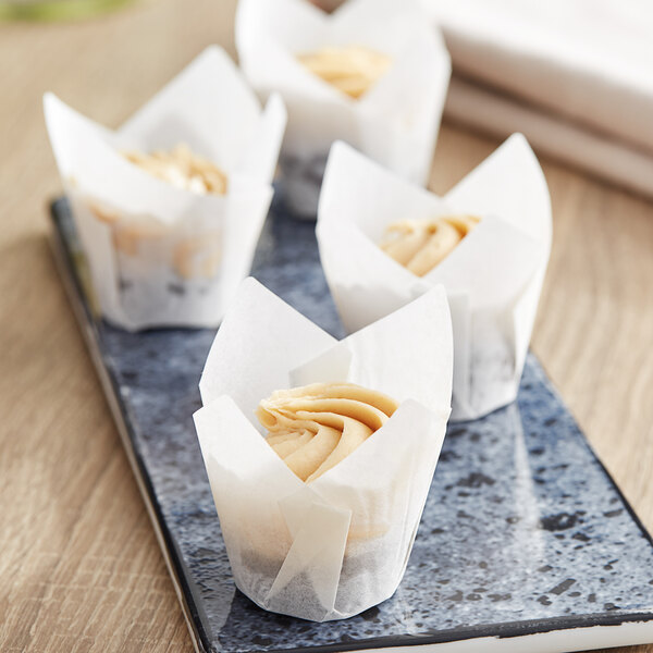 A group of Baker's Mark white mini tulip baking cups with three cupcakes on a plate.