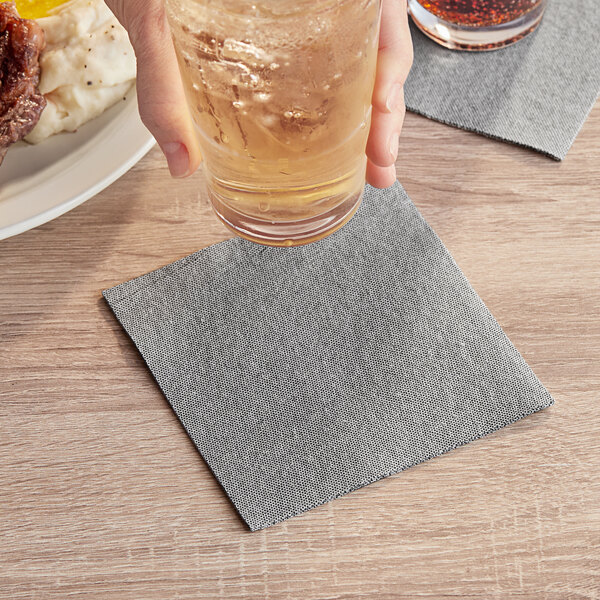 A hand holding a glass of liquid over a black Touchstone by Choice beverage napkin.