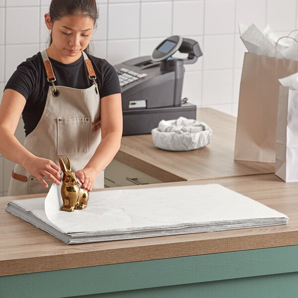 A woman in an apron cutting a light gray Lavex tissue paper sheet.