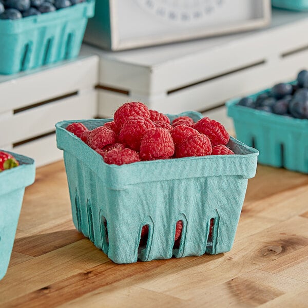 A green Pactiv berry basket filled with raspberries and blueberries.