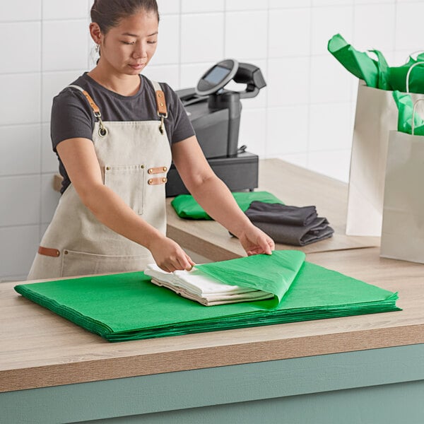 A woman in an apron cutting a green Lavex tissue paper sheet on a counter.