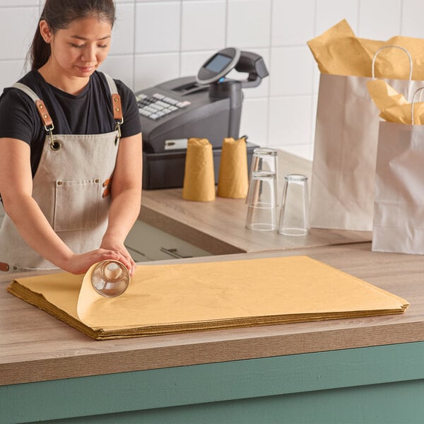 A woman in brown overalls cutting Lavex Kraft tissue paper on a counter.