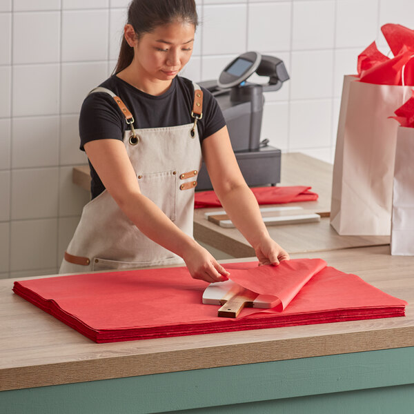 A woman cutting red Lavex tissue paper on a counter.