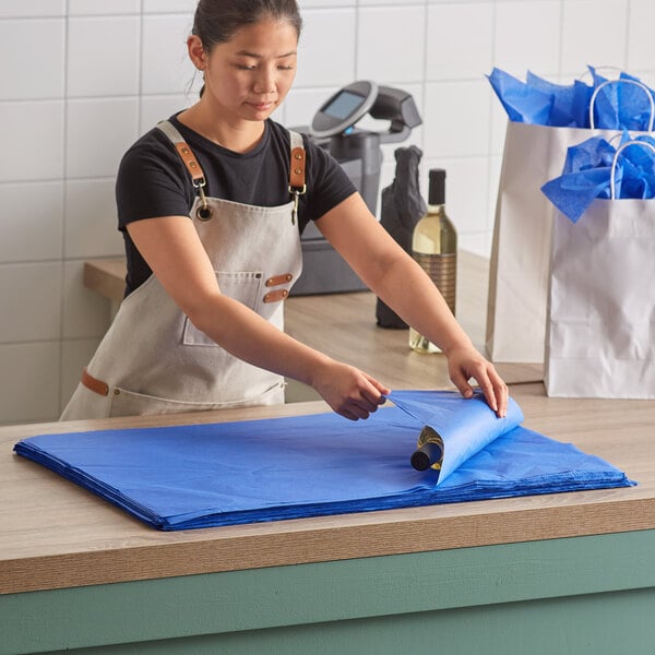 A woman in an apron folding a blue piece of paper.