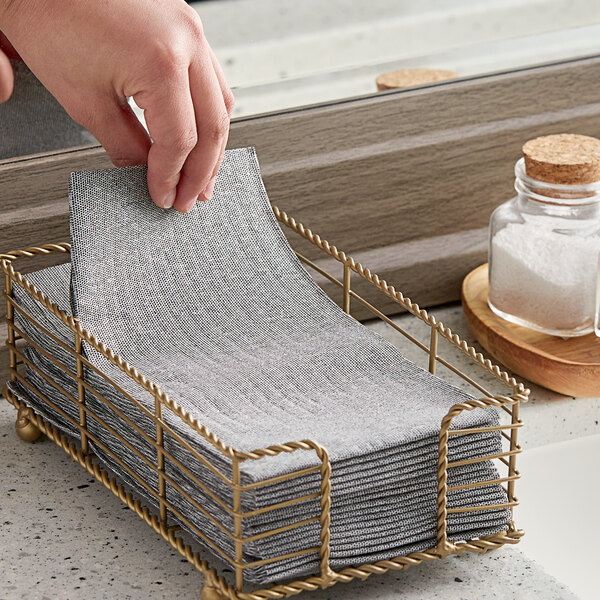A hand placing a Touchstone by Choice black linen-feel guest towel in a metal basket.