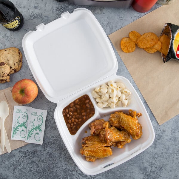 A white Dart styrofoam three-compartment takeout container with chicken wings, chips, and a drink inside.