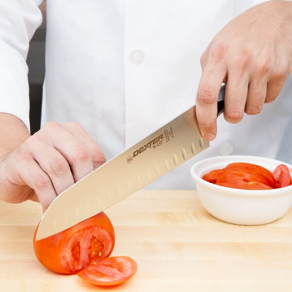 A person using a Dexter-Russell V-Lo Santoku chef knife to cut tomatoes.