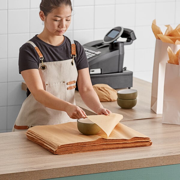 A woman in a white apron holding a bowl over a stack of Lavex Kraft Tissue Paper.