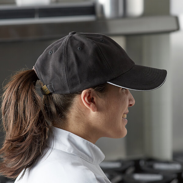 A woman in a Chef Revival black embroidered 6-panel baseball cap standing in a professional kitchen.