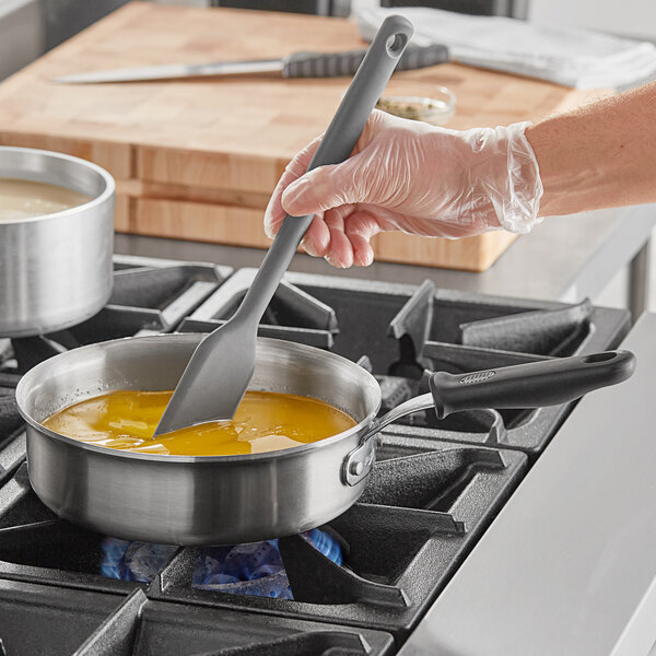 A person using a Vollrath saute pan with a spatula to cook.