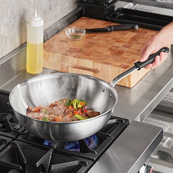 A person using a Vollrath stir fry pan to cook food on a stove.