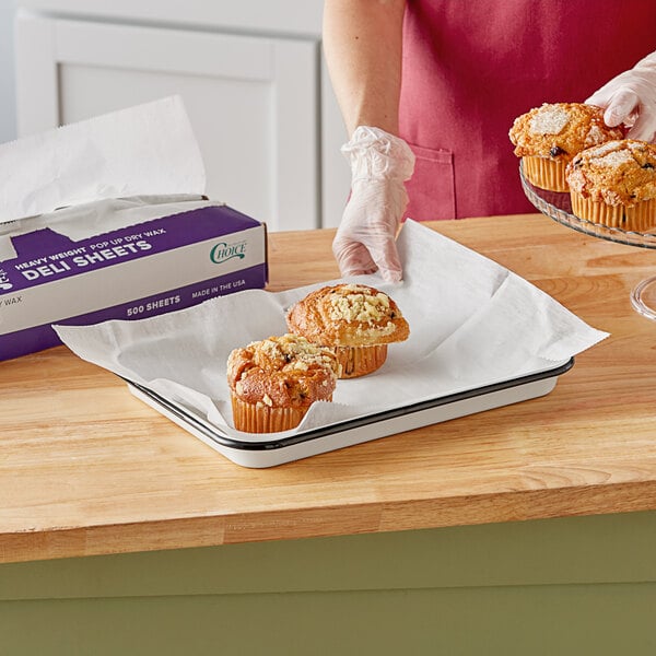 A hand using Choice deli wrap to pick up a muffin from a tray.