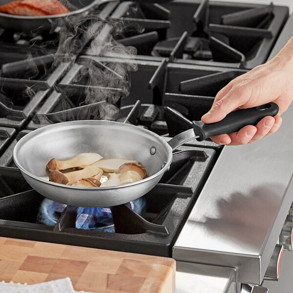 A hand holding a Vollrath Wear-Ever aluminum fry pan with a black handle over a stove.
