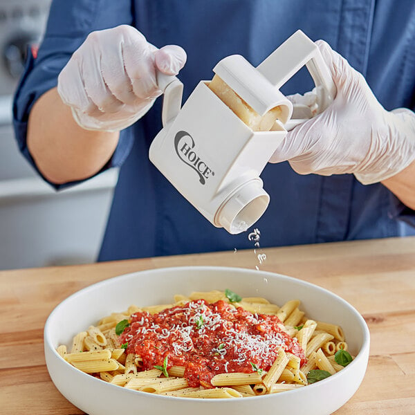 A person pouring cheese onto a bowl of pasta using a Choice rotary grater.