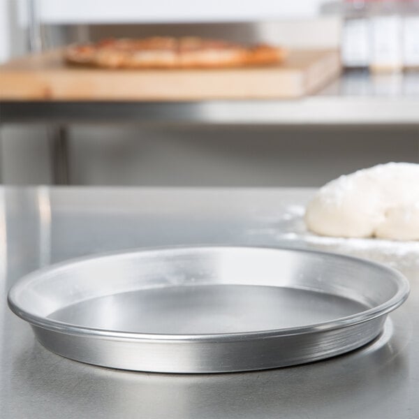 An American Metalcraft aluminum pizza pan on a counter with dough.