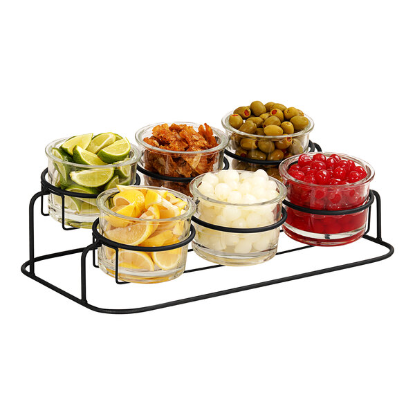 A black metal Cal-Mil 2-tier display with glass jars filled with lemons, limes, cherries, olives, and other food.