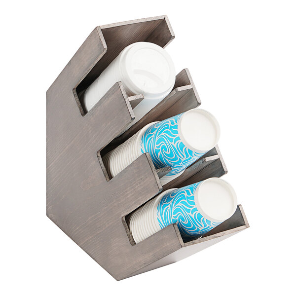 A Cal-Mil gray-washed pine wood countertop cup and lid organizer with three sections holding blue and white cups.