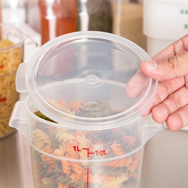 A hand using a Cambro translucent round lid to close a plastic container of pasta on a kitchen counter.