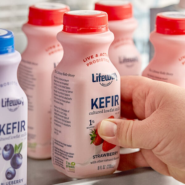 A person holding a close-up bottle of Lifeway Low-Fat Strawberry Kefir.