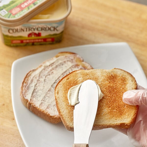 A hand spreading Country Crock butter on a piece of toast.