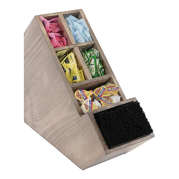 A Cal-Mil wooden stir stick and condiment display with removable dividers on a counter with different colored packets.