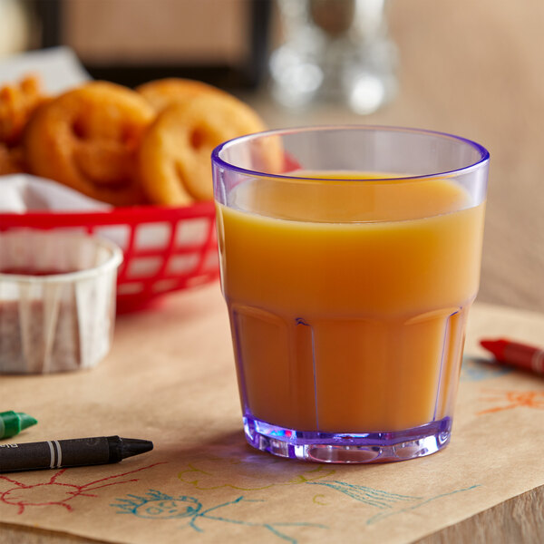 A close-up of a blue Bahama plastic tumbler filled with orange juice on a table with crayons.