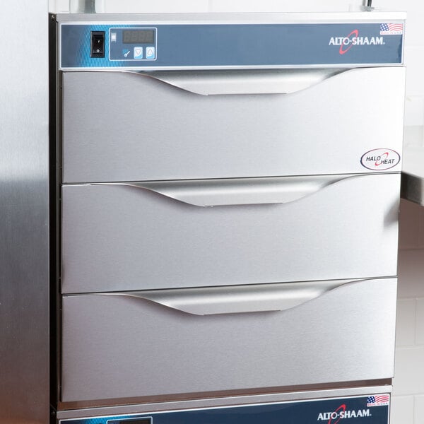 An Alto-Shaam 3 drawer warmer on a counter with open stainless steel drawers.