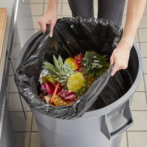 A woman's hands putting a Lavex trash bag full of food into a trash can.