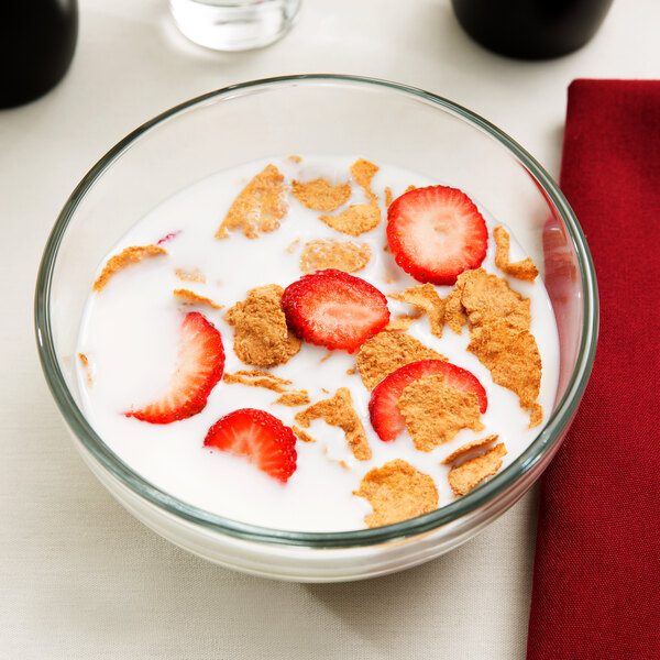A close-up of a Libbey glass cereal bowl filled with milk and cereal with strawberries.