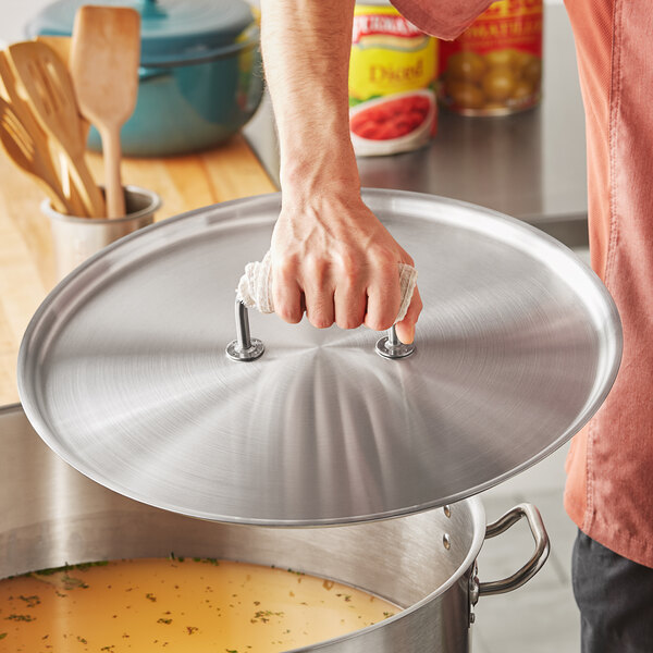 A person using a Vollrath stainless steel lid to cover a pot on a counter.