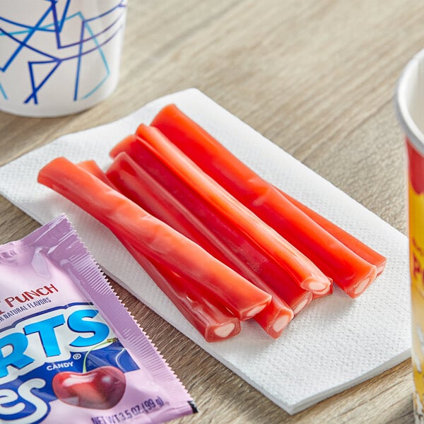 A white cup of SweeTarts Cherry Punch Ropes next to a group of red sticks.