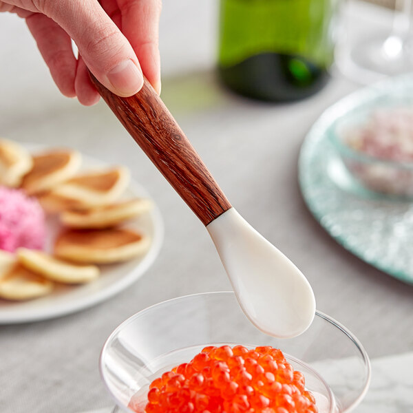 A hand holding an Acopa Mother of Pearl spoon over a bowl of red caviar.