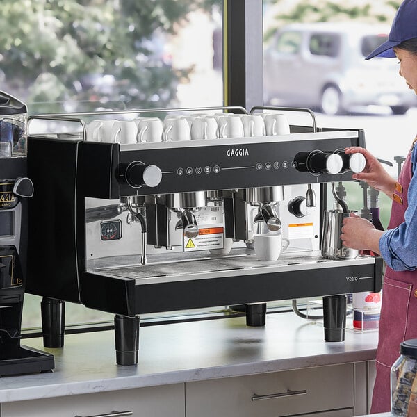 A woman using a Gaggia Vetro black espresso machine to prepare coffee.