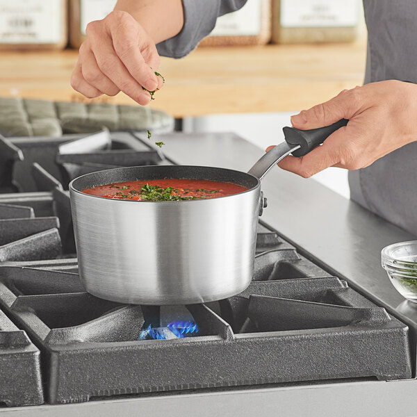A woman cooks soup in a Vollrath Wear-Ever sauce pan on a stove.