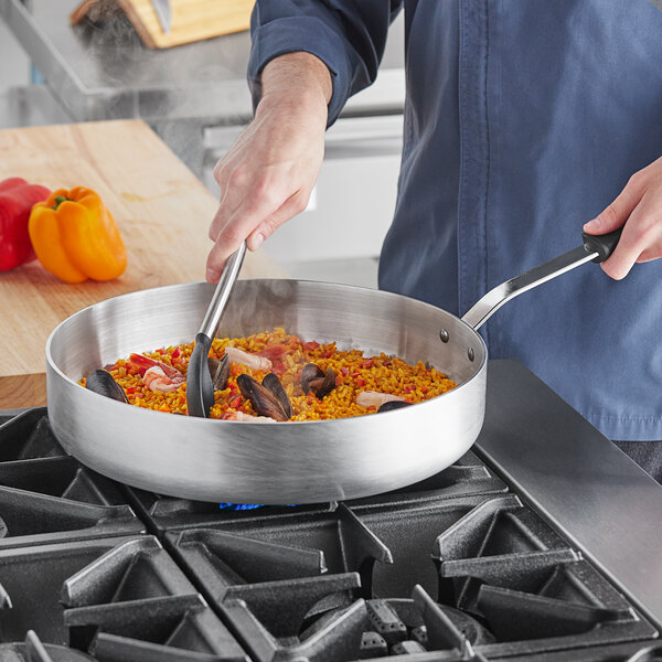 A person cooking rice and seafood in a Vollrath Wear-Ever aluminum saute pan.