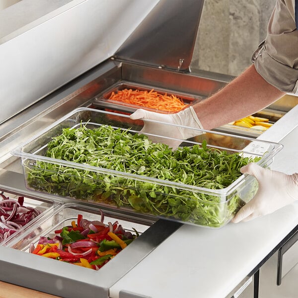 A person in gloves using a Choice clear polycarbonate food pan to hold vegetables at a salad bar.