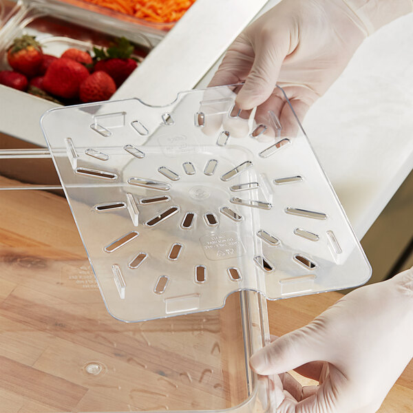 A person in gloves is using a Choice clear polycarbonate drain tray to cut vegetables on a counter.