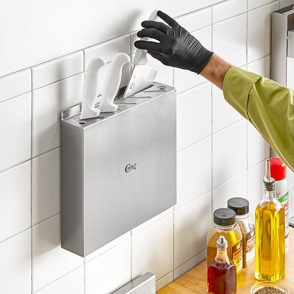 A person putting knives in a stainless steel wall-mount knife rack.