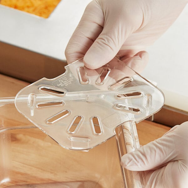 A gloved hand holding a Choice clear polycarbonate drain tray with holes.