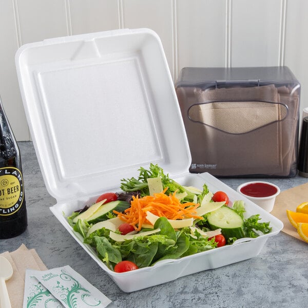 A salad in a Dart white foam takeout container with a hinged lid.