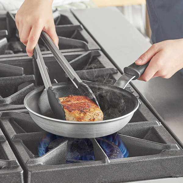 A person cooking meat in a Vollrath Wear-Ever non-stick fry pan.
